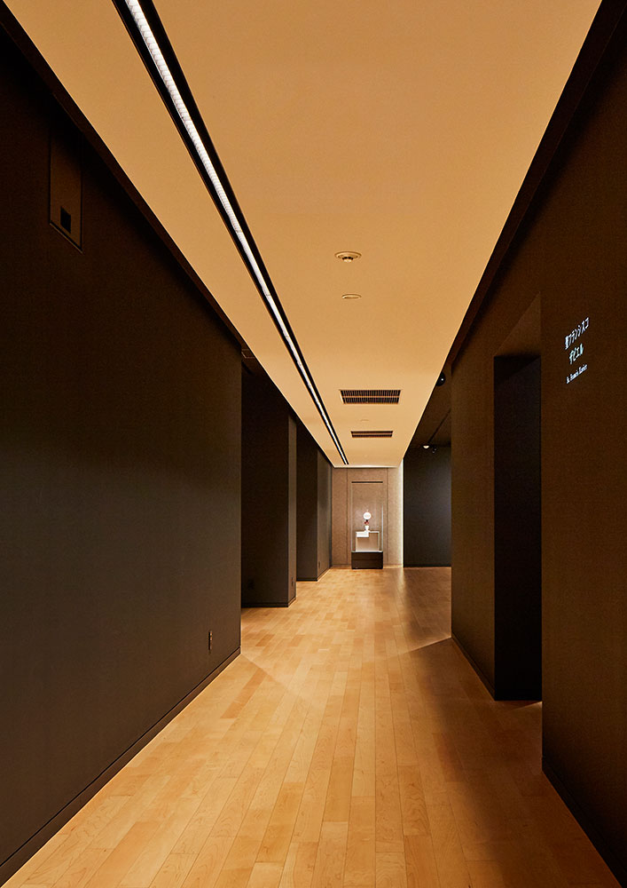 既存の細長い建築形状を活かした、ライン照明が印象的な2階展示室の通路部。両側に展示スペースが並ぶ。