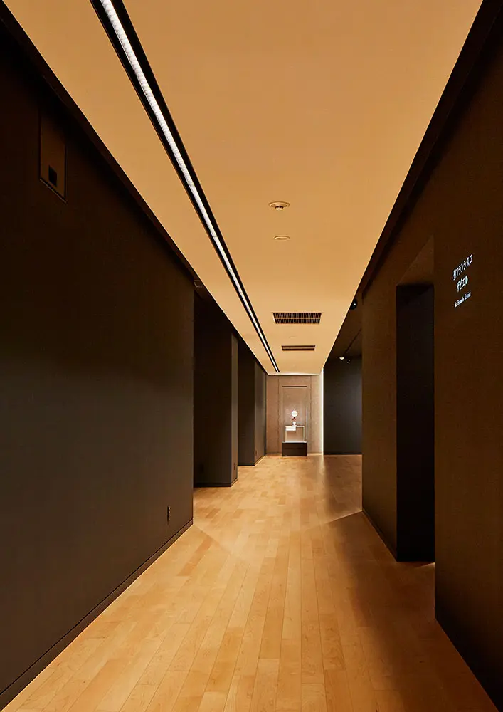 The corridor to the second floor exhibition room features impressive linear lighting that makes use of the existing slender architectural shape. Exhibition spaces are lined on both sides.