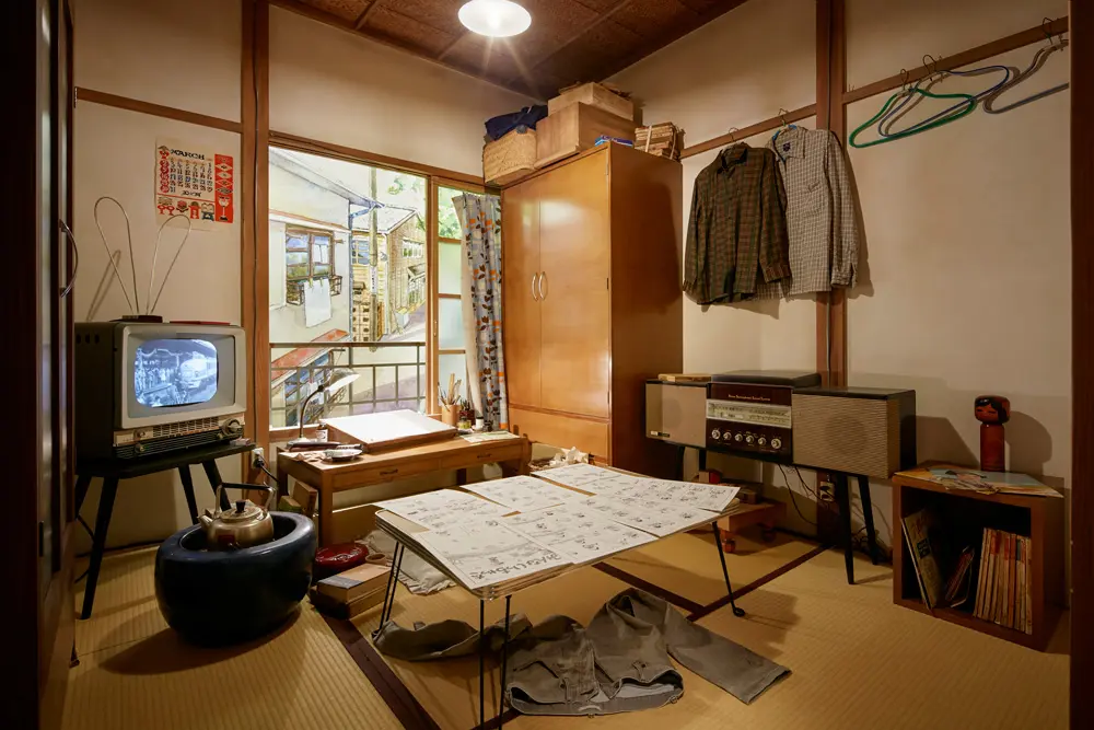 よこたとくおさんの部屋。テレビからは当時のニュース映像やCMが流れ、２階の空間全体に当時の空気感を伝えている