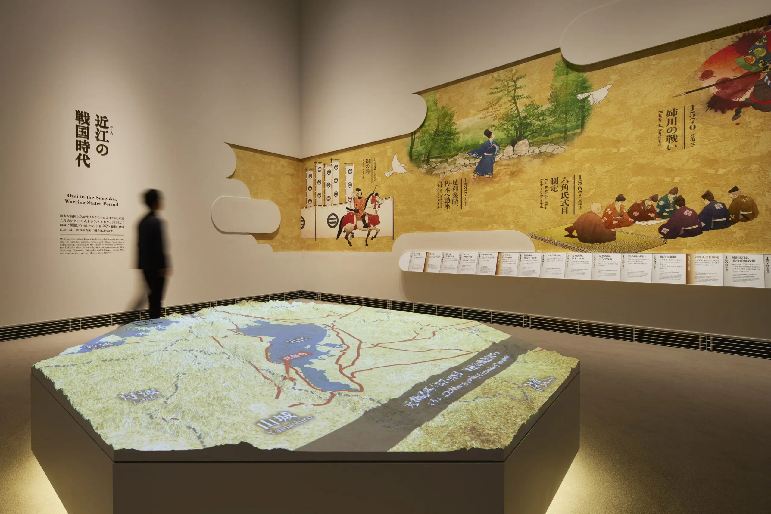 The timeline graphic on the wall and projection mapping onto the white model explain "The Sengoku Period in Omi" and "The Life of Oda Nobunaga."