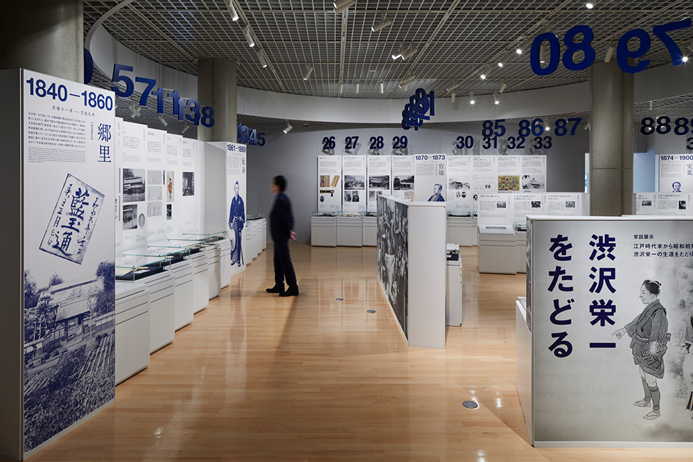 天吊りの年齢サインと展示ユニットによる構成。一覧性を重視した配置によって、空間構成と順路が直感的に理解できる。