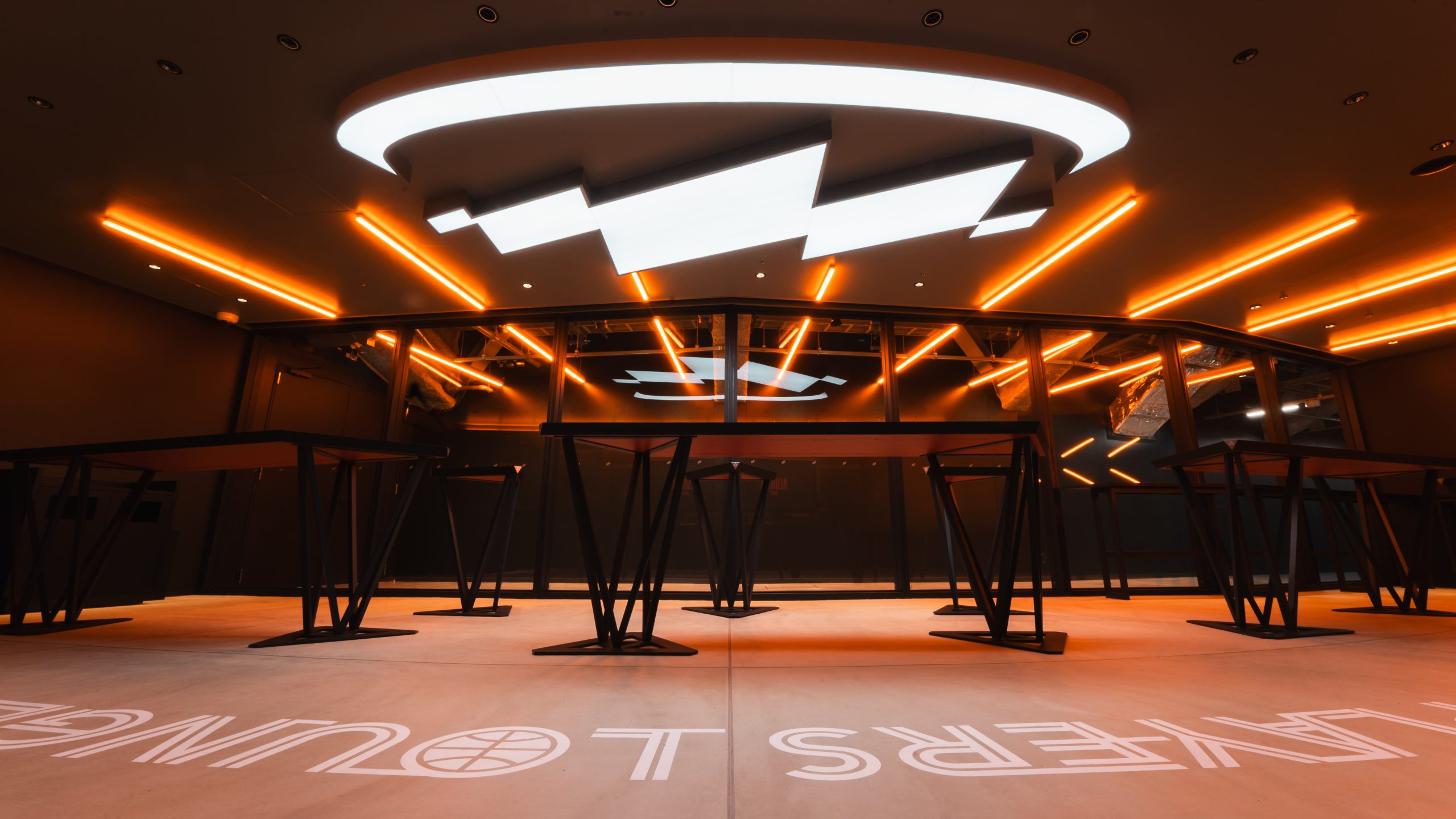 ガラスを挟んで選手動線から伸びるライン照明と天井面に大きく表現されたアリーナロゴ