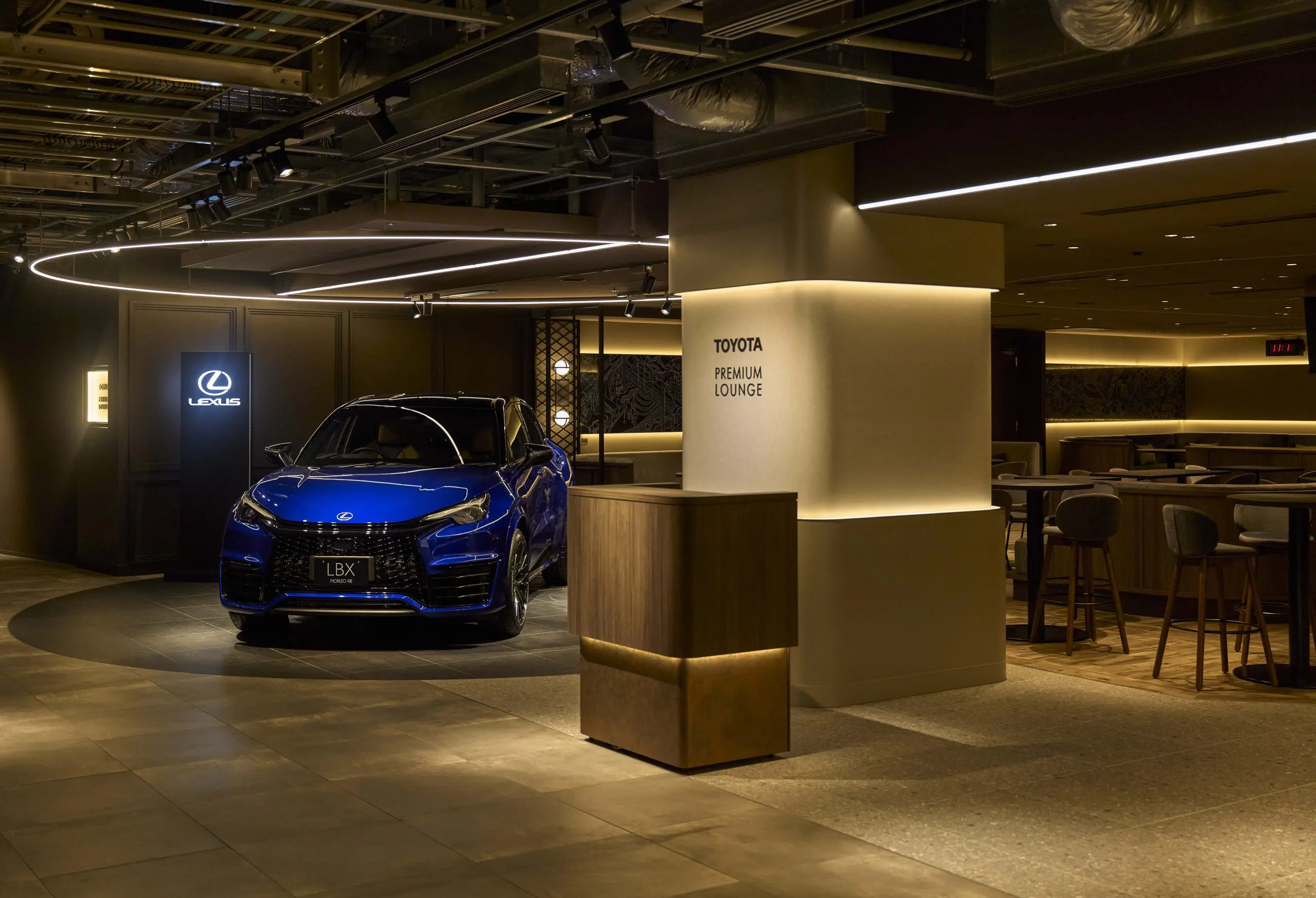 A lounge where car exhibitions and dining areas coexist comfortably. The high counter seats near the reception are perfect for enjoying a quick meal between games.