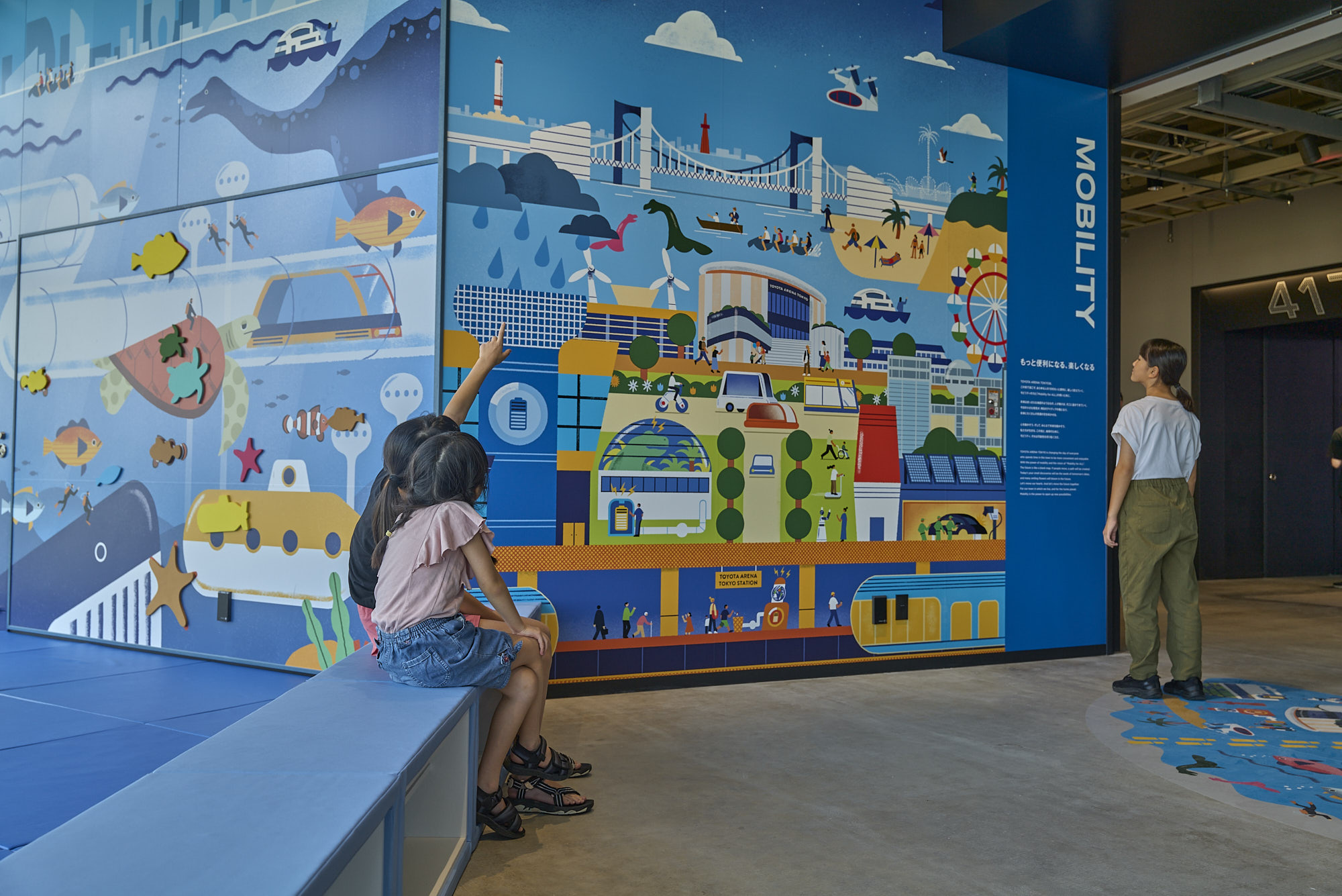 壁面のイラストは未来の街を表現している。人々の振る舞いも、エネルギーの生産方法も多様である