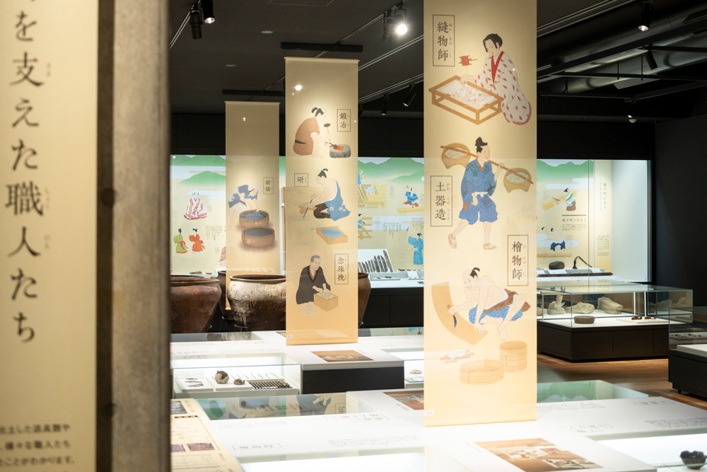 発掘資料から伺える多彩な職人たちの様子をイラストで再現。遺物に加え人々の気配を展示空間で感じられるようにした