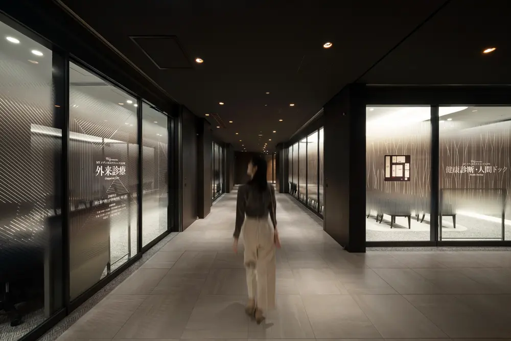 The approach to the medical examination area and outpatient area. Each examination area stands out brightly in white, contrasting with the black corridor on the ceiling.