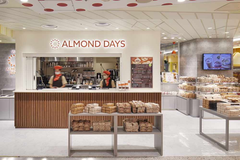 Glico ALMOND DAYS：中央ドリンクカウンターに木質や石材を設えることで素材へのこだわりを表現した店舗。アーモンドの魅力を発信する場として展開し、さまざまな商品提供をしていただけるように可変性のある什器で構成している
