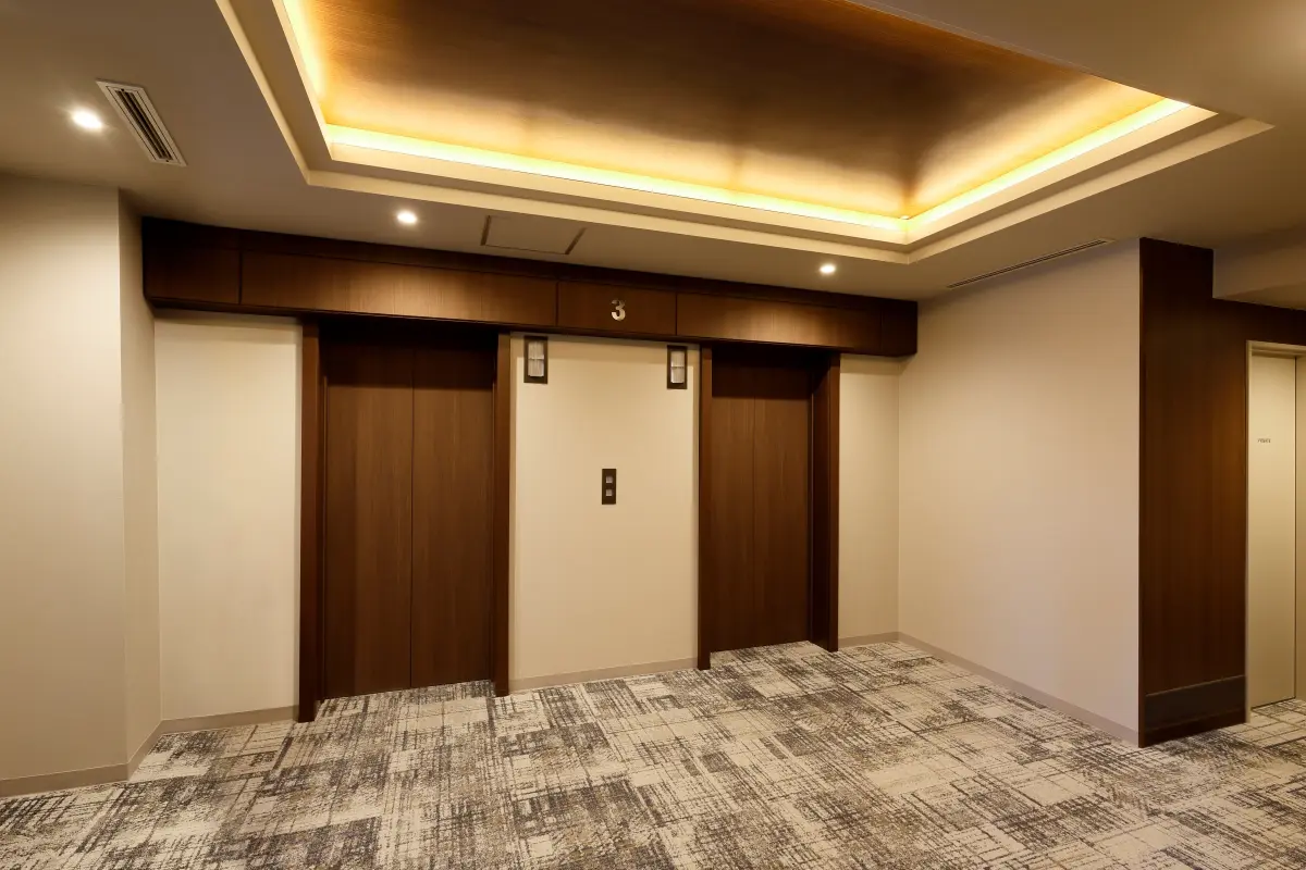 By using dark wood as the key material and revising the lighting plan, the elevator hall was efficiently updated into a high-quality space.